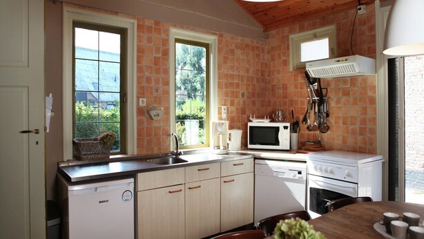 A kitchen with a wooden ceiling, a white stove, a microwave, and a sink. There are cabinets and a window with a view of greenery. - Pet-Friendly Farmhouse (Eede)