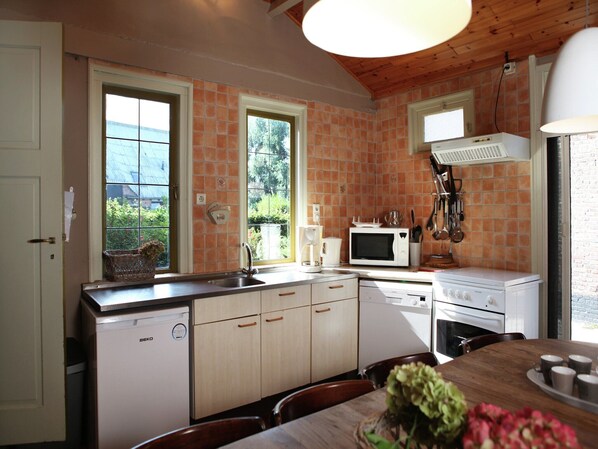 A kitchen with a wooden ceiling, a white stove, a microwave, and a sink. There are cabinets and a window with a view of greenery. - Pet-Friendly Farmhouse (Eede)