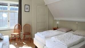 A bedroom with two beds, a wooden chair, a bedside table with a lamp, and a window with curtains. - Pet-Friendly Farmhouse (Eede)