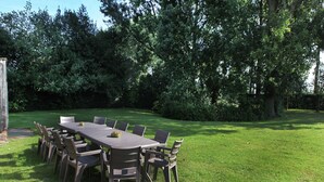 An outdoor dining area with a rectangular table and multiple chairs, surrounded by a grassy lawn and trees. - Pet-Friendly Farmhouse (Eede)