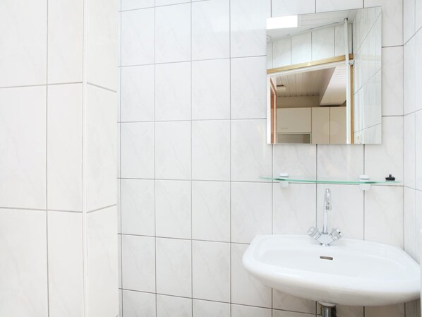 A bathroom with white tiles, a white sink, a glass shelf, and a mirror. - Farmhouse in Ulicoten near Forest Trails (Ulicoten)