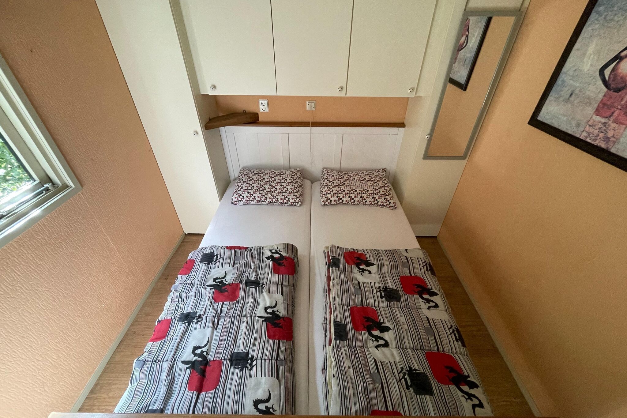 Ein kleines Zimmer mit einem Bett, einem Fenster und einem Wandregal.