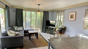 A living room with a sofa, a TV, a dining table, and a view of the outdoors.