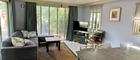 A living room with a sofa, a TV, a dining table, and a view of the outdoors.