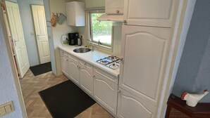 A compact kitchen with white cabinets, a gas stove, a sink, and a window.