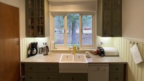 A kitchen with a sink, countertop, cabinets, and a window with a view of trees. - Hideaway: Sauna, Tennis & Trampoline (Oploo)