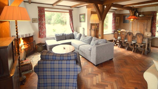 A cozy living room with a fireplace, a sofa, a plaid chair, and wooden beams on the ceiling. - Hideaway: Sauna, Tennis & Trampoline (Oploo)