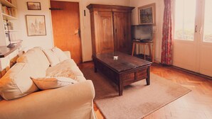 A cozy living room with a wooden coffee table, a sofa, a television on a stand, and a bookshelf filled with books. - Hideaway: Sauna, Tennis & Trampoline (Oploo)