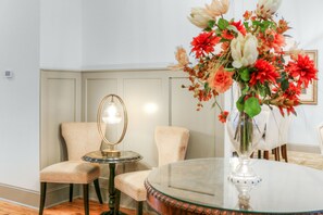 Et værelse med et rundt glasbord, to stole, en vase med blomster og en lampe.