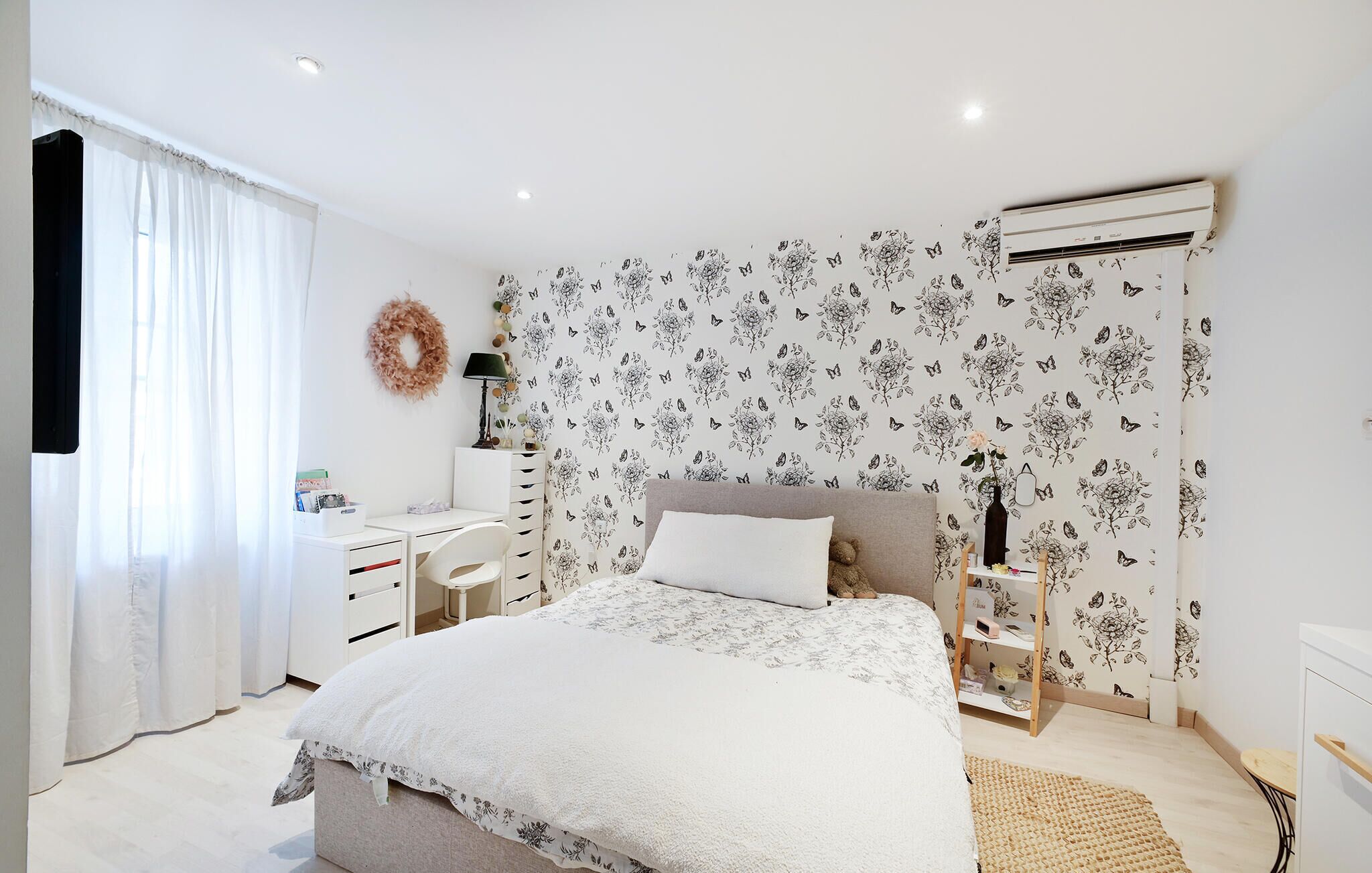 A bedroom with a bed, a desk, a chair, a dresser, and an air conditioning unit.