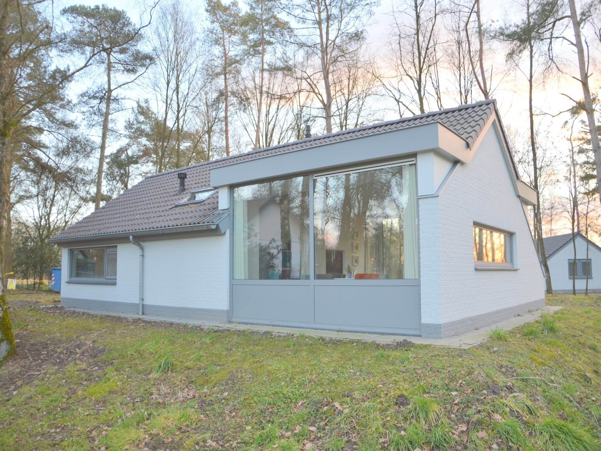 Une maison moderne, de plain-pied, dotée de grandes fenêtres et d’un toit en pente, entourée d’arbres.