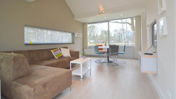 A modern living room with a brown leather sofa, a white coffee table, and a dining area with a table and chairs.