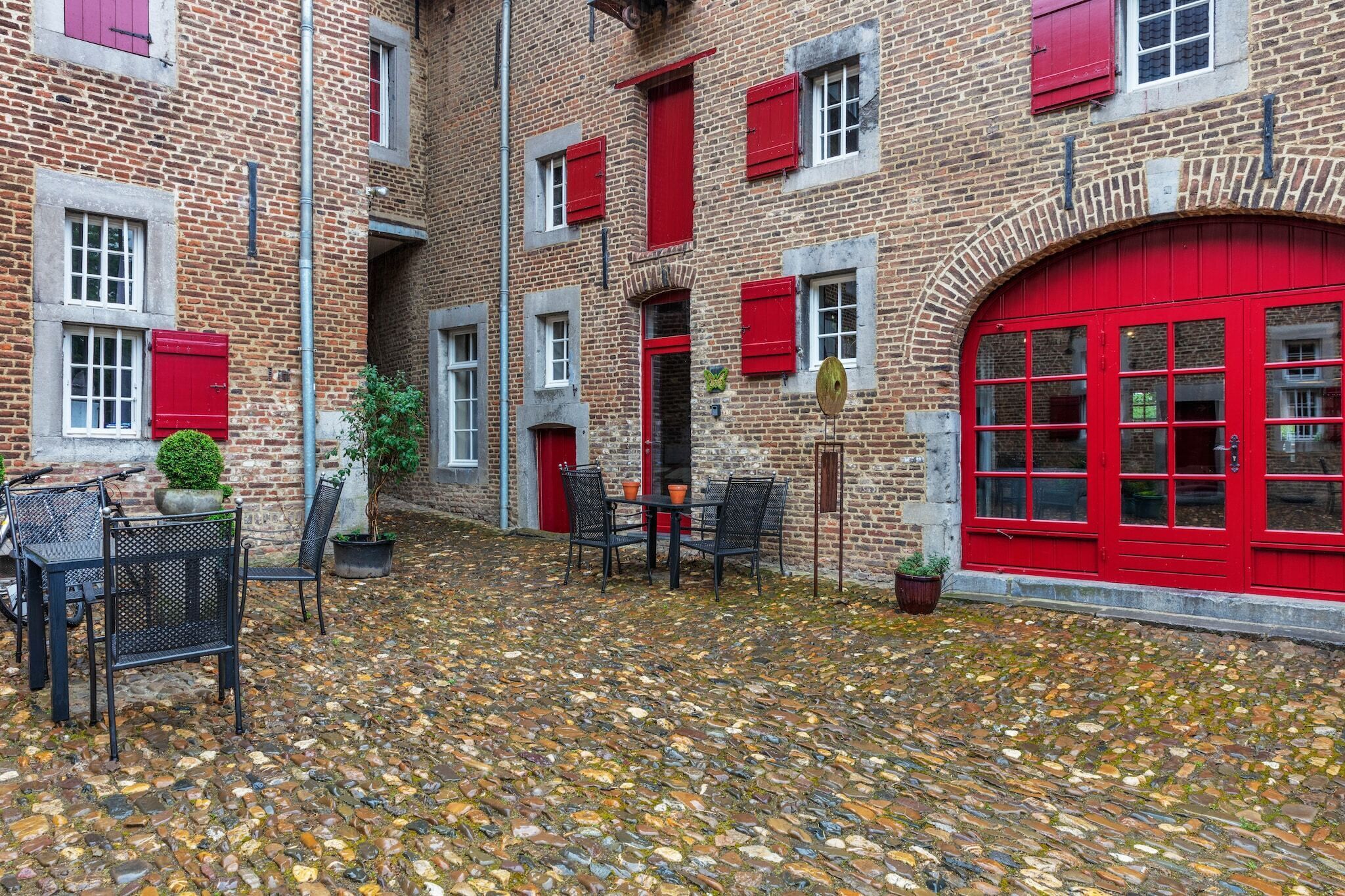 Ein Innenhof mit Kopfsteinpflaster, Backsteinmauern, roten Fensterläden und einer roten Tür.