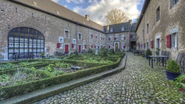 Een binnenplaats met geplaveide paden, bakstenen gebouwen en een tuin met bankjes.