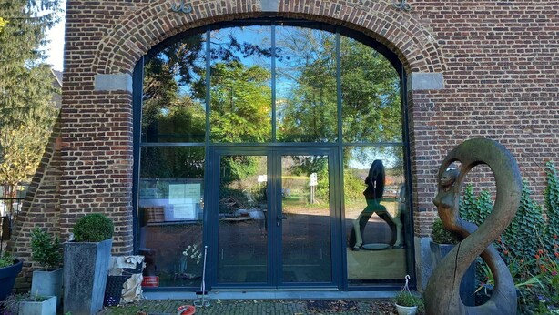 A brick building with a large arched entrance, a glass door, and a sculpture of a swan. - Group Retreat in Mesch (Mesch-Eijsden)