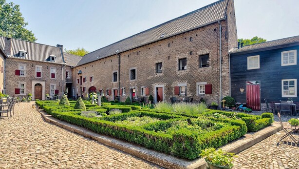 Ein Innenhof mit einem Kopfsteinpflasterweg, einem Backsteinhaus mit roten Fensterläden und einem gepflegten Garten.
