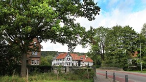 Ein traditionelles Fachwerkhäuschen mit einer Steinsäule vor der Fassade, einem gepflasterten Bürgersteig und einer Straße mit Poller.
