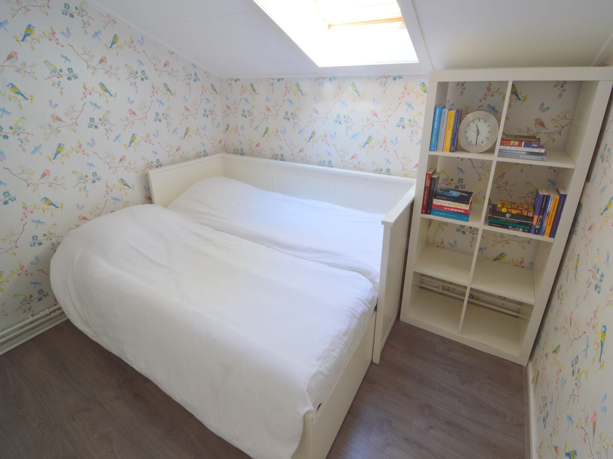 A bedroom with a bunk bed, a skylight, a bookshelf with books, and patterned wallpaper.