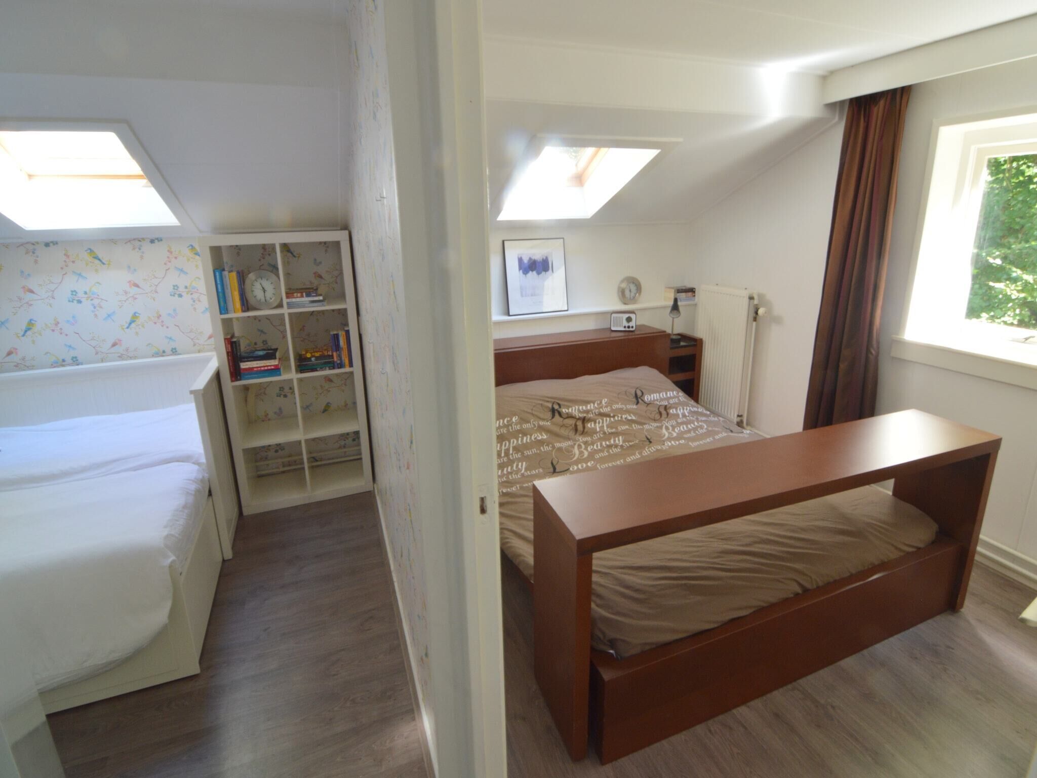 A bedroom with a bunk bed, a wooden desk, a bookshelf, a window with curtains, and a skylight.