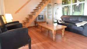 Un salon avec un escalier en bois, un canapé en cuir noir, une table basse en bois et un téléviseur.