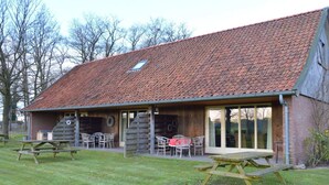 Un bâtiment rustique avec un toit en tuiles, un patio couvert avec des sièges extérieurs et des tables de pique-nique.