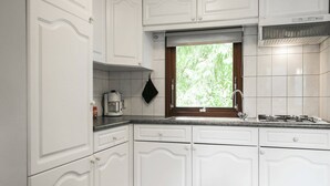 Een keuken met witte kasten, een raam met uitzicht op groen, een fornuis en een koffiezetapparaat.