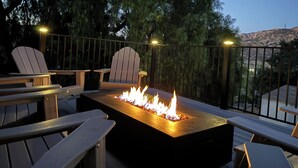 Eine Terrassenanlage im Freien mit integriertem Feuerplatz, zwei Adirondack-Stühlen und einer Geländer.