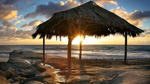 Ein Strand mit einer ummauerten Hütte, Meereswellen und einem Sonnenuntergang.