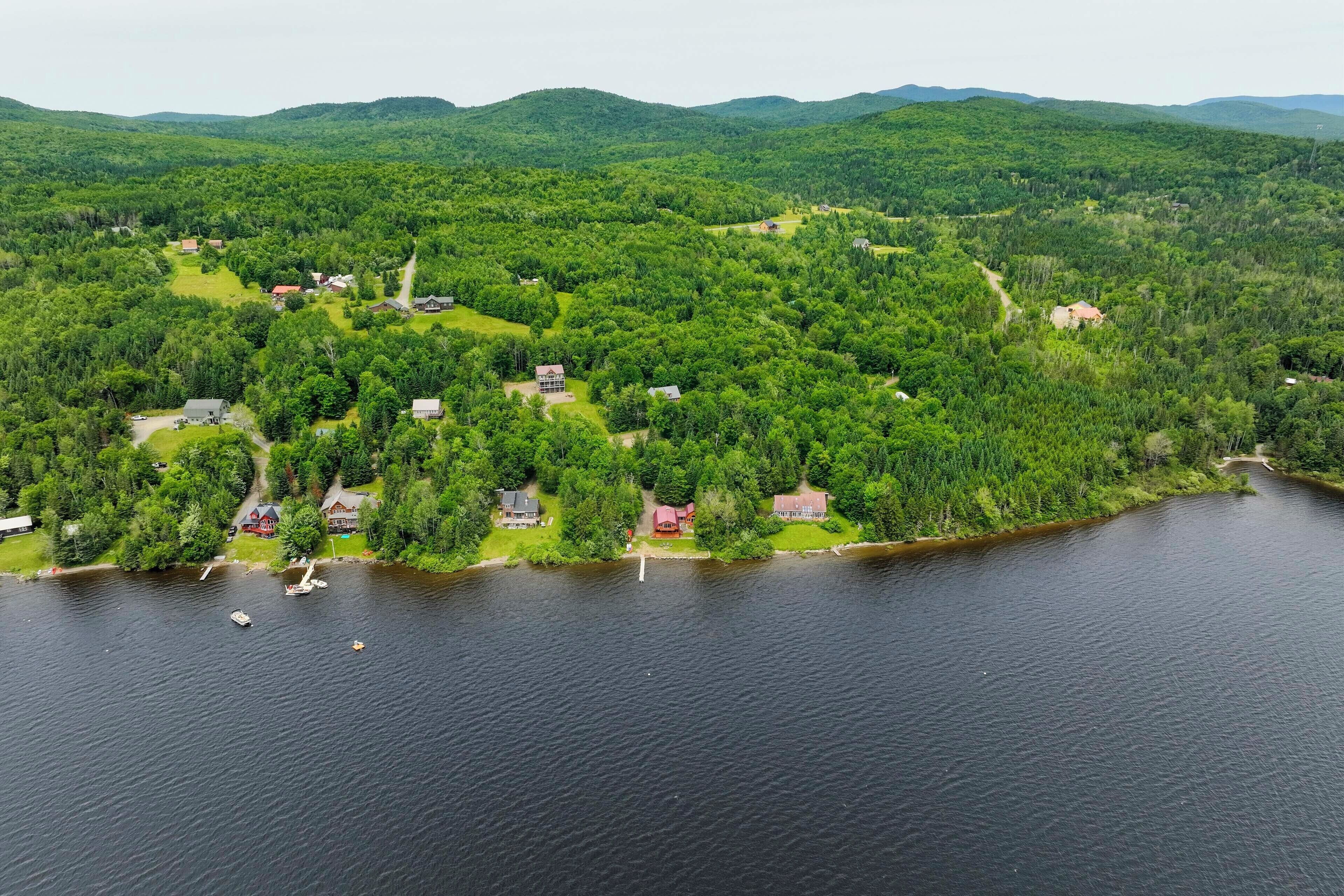 An aerial view of a lakeside property with multiple houses, a dock with boats, and surrounding forested hills.