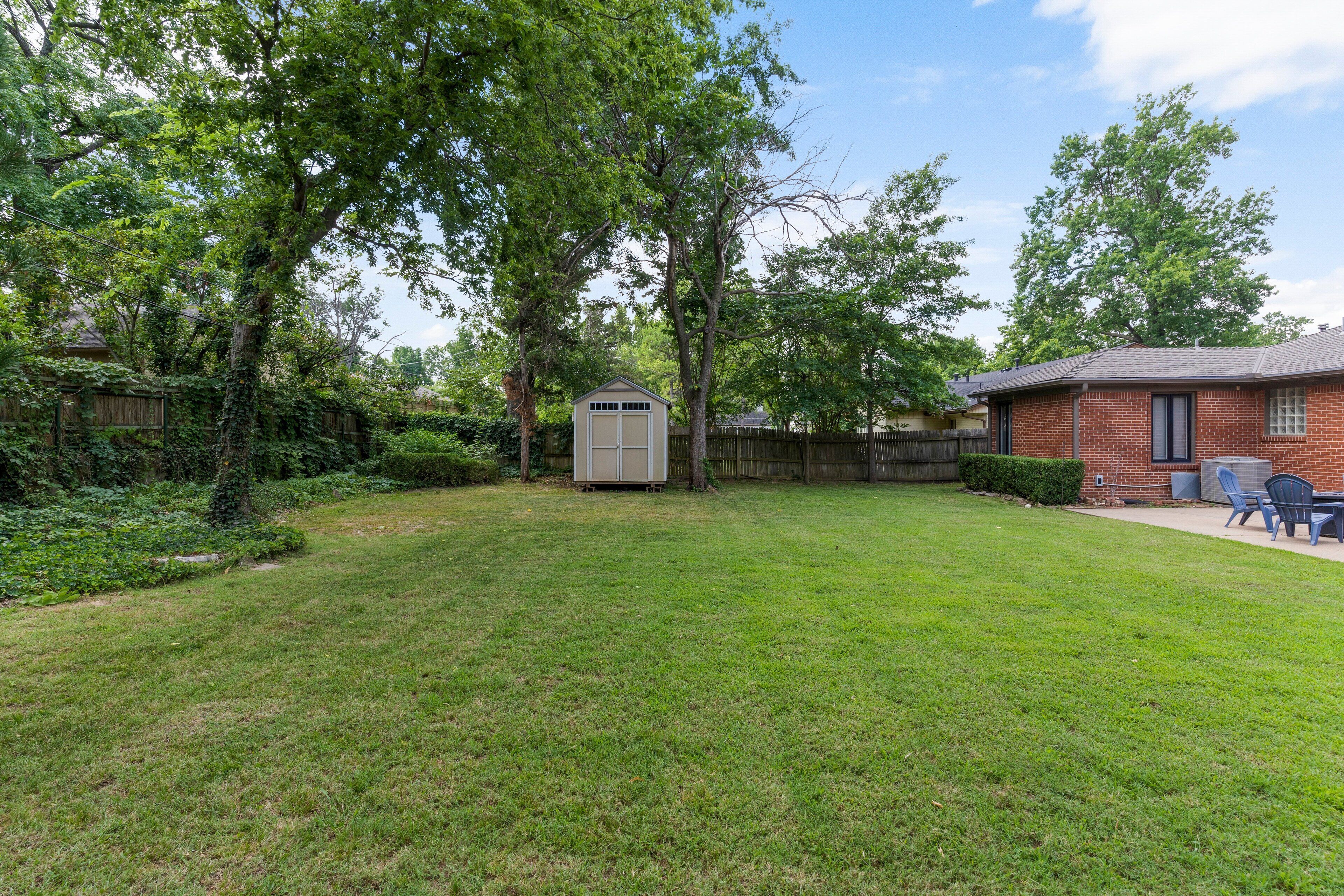 A backyard with a shed, a brick house, and a lawn.
