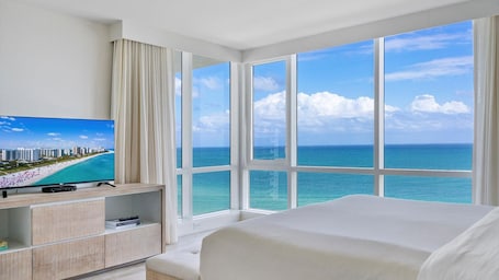 A hotel room with a large window offering a view of the ocean and a cityscape.