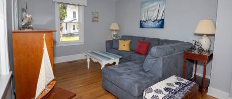 A living room with a grey sofa, wooden coffee table, and a small wooden desk with a model sailboat.