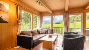 A cozy room with a wooden ceiling, large windows, a sofa, a coffee table, and a chair. - Chalet in St. Georgen (St.Georgen ob Murau)