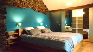 A bedroom with a stone wall, a bed with a blue bedspread, two bedside lamps, and a wooden nightstand. - Champlon Villa near Forest (Champlon)