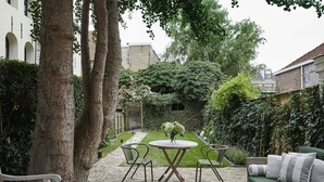 A courtyard with a round table and chairs, surrounded by trees and a hedge. - Grand townhouse in Harlingen near Beach (Harlingen)