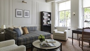 A living room with a plaid sofa, a round coffee table with books and a plant, a bookshelf, a white armchair, and a window with a view of the street. - Grand townhouse in Harlingen near Beach (Harlingen)