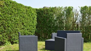 Terrassenmöbel aus Rattan in einer grünen Rasenfläche, im Hintergrund dichte Hecken.