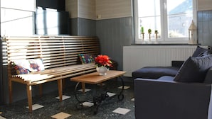 Ein gemütliches Wohnzimmer mit einer Holzbank, einem kleinen Tisch mit einer Vase, einem Sofa und einem Fenster mit Blick.