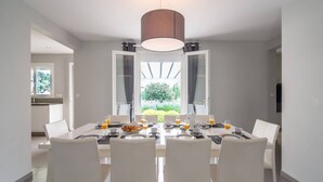 A modern dining area with a large table set for six, white chairs, and a central hanging light fixture.