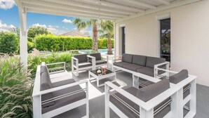 An outdoor patio with white furniture, a pool, and a view of a green landscape.