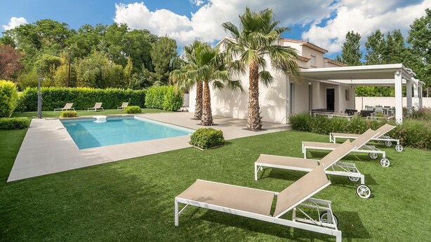 A pool area with lounge chairs, a pergola, and palm trees.