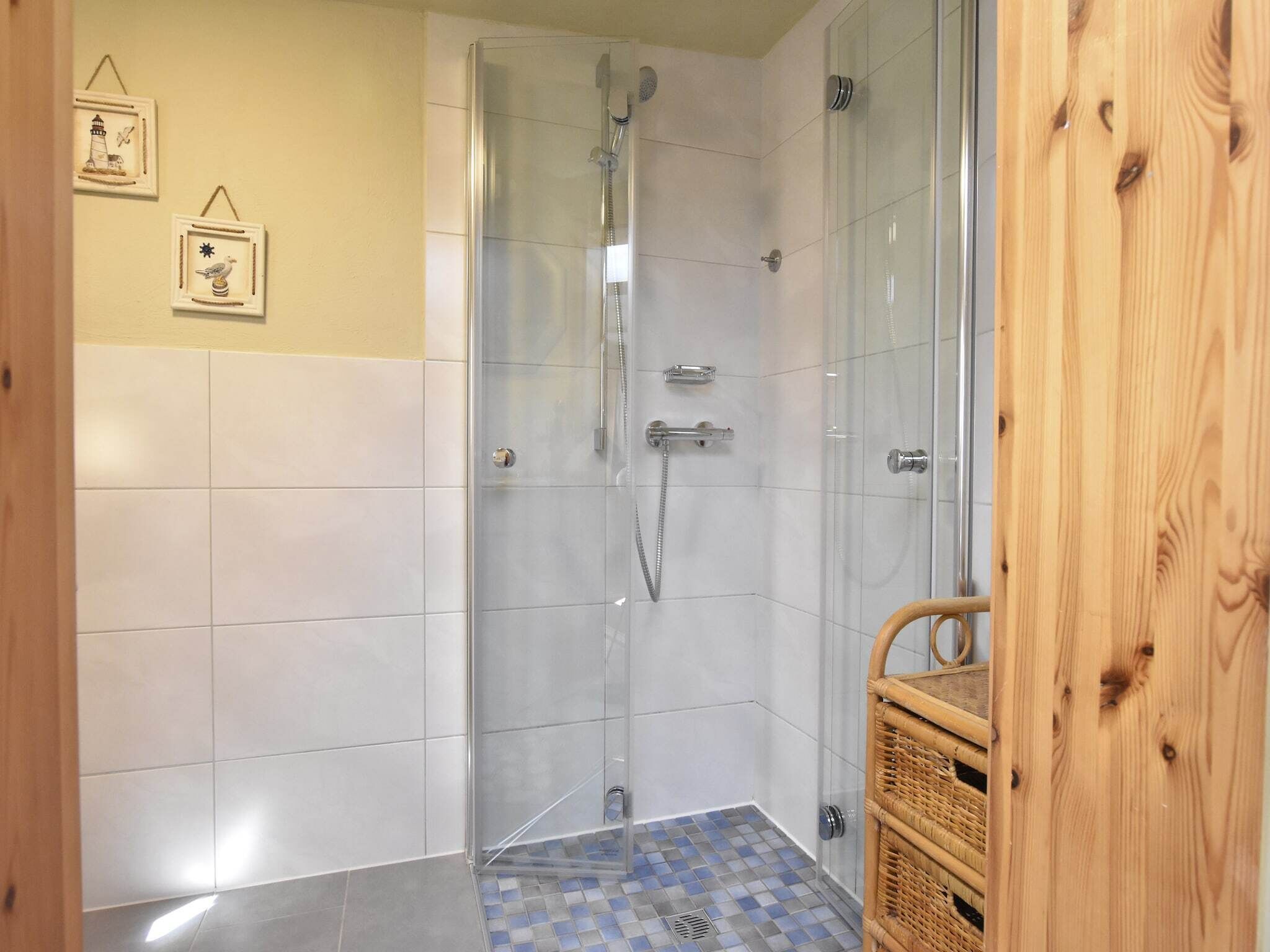Een douchecabine met glazen wanden, een chroomdouchekop en een handdouche, betegelde wanden en een zwart-wit betegelde vloer.
