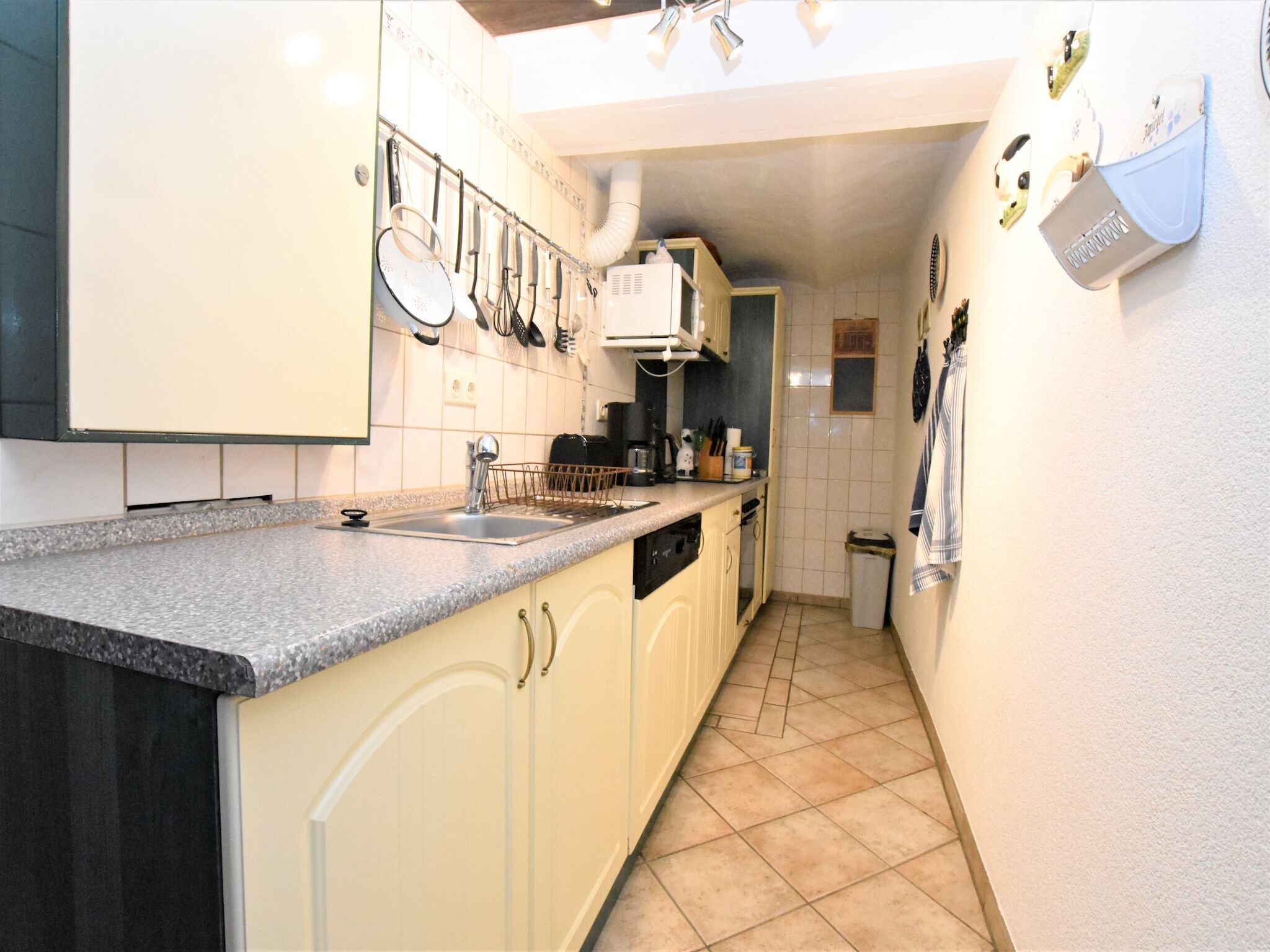 A narrow kitchen with a granite countertop, white cabinets, and a tiled backsplash.