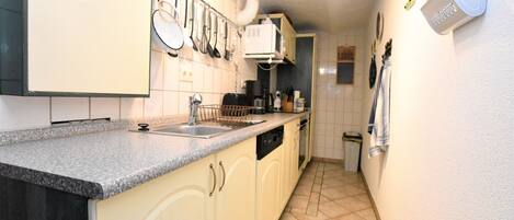 A narrow kitchen with a granite countertop, white cabinets, and a tiled backsplash.