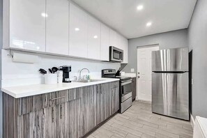 A modern kitchen with white cabinets, a stainless steel refrigerator, and a microwave. - Modern 1BR Near Pompano Beach | Steps to Sand (Pompano Beach)