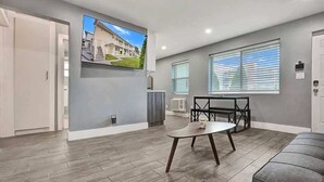 Ein modernes Wohnzimmer mit einem an der Wand befestigten Flachbildfernseher, einem Esstisch mit Stühlen und einem grauen Sofa.