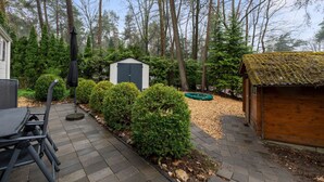 A patio with a table and chairs, surrounded by a garden with a shed and a wooden structure. - Beautiful Holiday Chalet in Emst with a private garden (Emst)