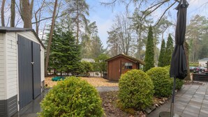 A small wooden cabin surrounded by well-maintained bushes and trees, with a paved path leading to it. - Beautiful Holiday Chalet in Emst with a private garden (Emst)
