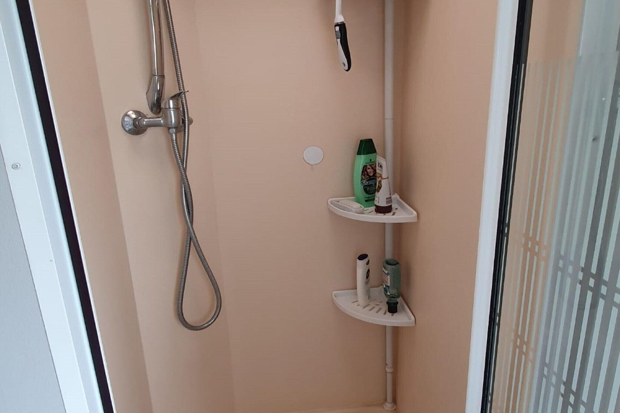 A shower area with a handheld showerhead, a wall-mounted faucet, and a shelf with toiletries.