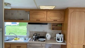 A compact kitchen with wooden cabinets, a sink, a stove, and a coffee maker. - Auw Farm Life Escape (Auw)